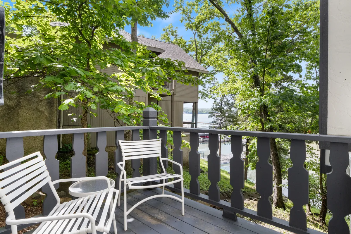 A tranquil balcony with white chairs positioned to overlook the lake, perfect for morning coffee or evening gatherings. The view extends over the water, promising shared moments in a scenic setting.