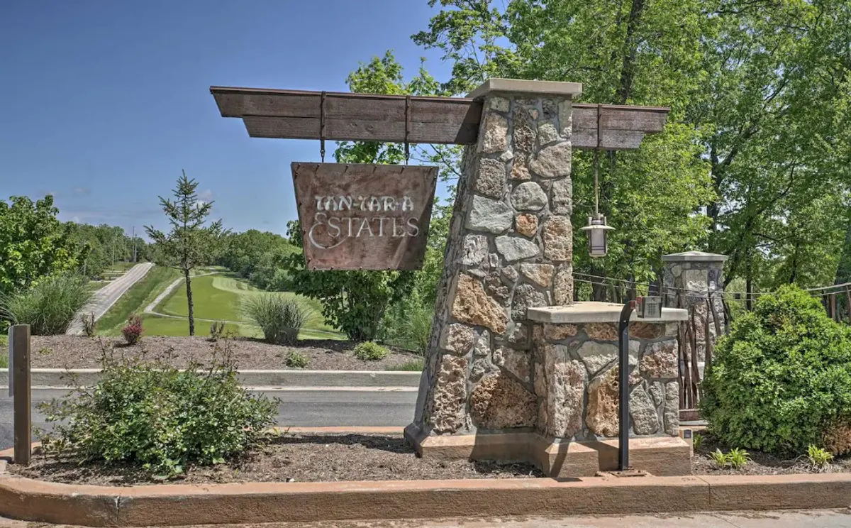 This image captures the welcoming stone structure and wooden sign at the entrance to the estate, framed by lush landscaping and a path leading inward. The setting exudes a sense of arrival and anticipation, hinting at the adventure and natural beauty that await just beyond.