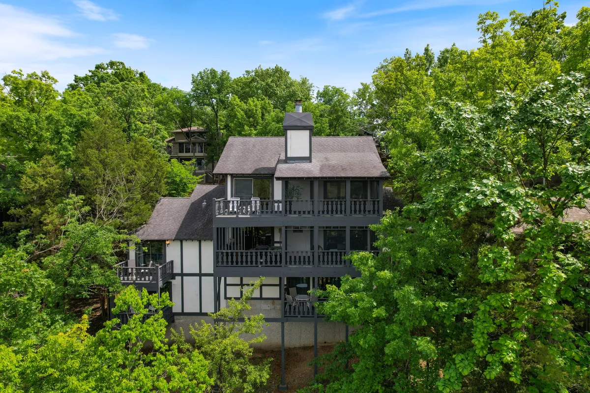 An exterior shot emphasizing the house's structure, spacious balconies, and the surrounding wooded landscape. The multiple balconies invite relaxation and offer spaces for enjoying sunsets and the beauty of the lakeside environment, supporting the narrative of a refined, amenity-rich retreat.