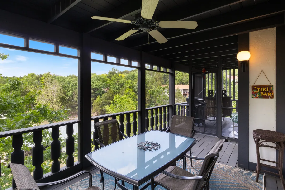 A bright, casual space featuring a glass table and seating, ceiling fan, and a view of lush trees through large windows or a screened-in area, suggesting a direct transition to the outdoors. The setting feels ideal for informal chats or enjoying morning coffee with nature.