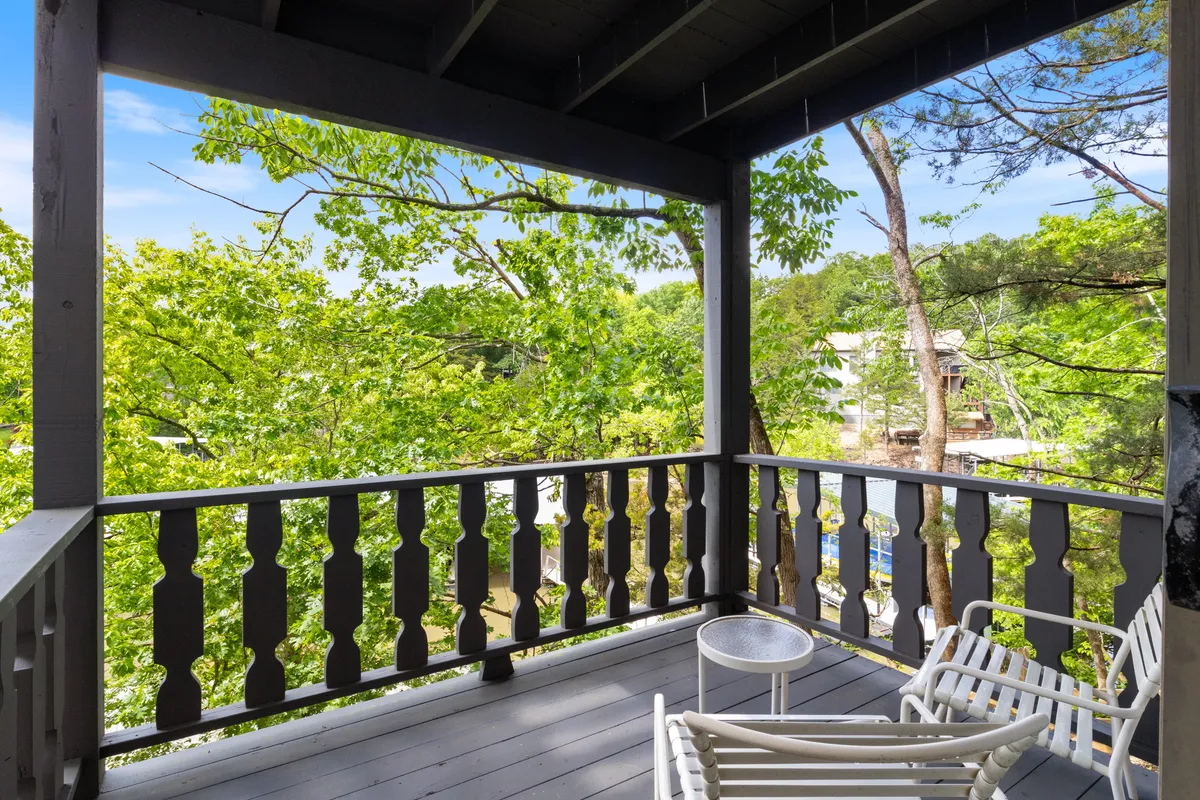 A serene balcony scene featuring white chairs and a round table, overlooking dense green treetops. The inviting outdoor seating area is ideal for morning coffee or evening relaxation, providing a direct visual link to the scenic lake views and tranquil atmosphere mentioned in the section.