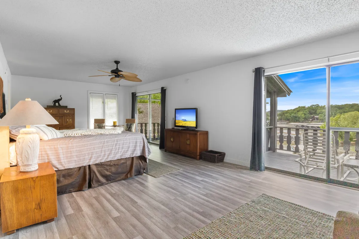 A serene bedroom featuring a king-sized bed with plush bedding, large windows that let in natural light, a television mounted for convenient viewing from bed, and elegant wooden furniture. The atmosphere is tranquil and designed for both comfort and privacy.