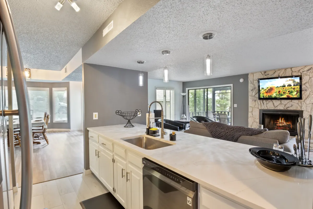 An inviting open-concept space blending a contemporary kitchen island, a cozy fireplace, large windows, and a stylish dining area ready for gatherings. The space radiates warmth and hospitality, perfect for shared meals and entertaining.