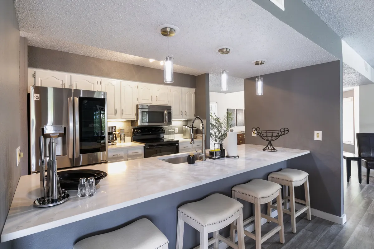 A spacious, modern kitchen featuring a large island with bar stools, gleaming stainless steel appliances, and ample counter space. The scene suggests active use, with an inviting atmosphere for both serious cooking and socializing.