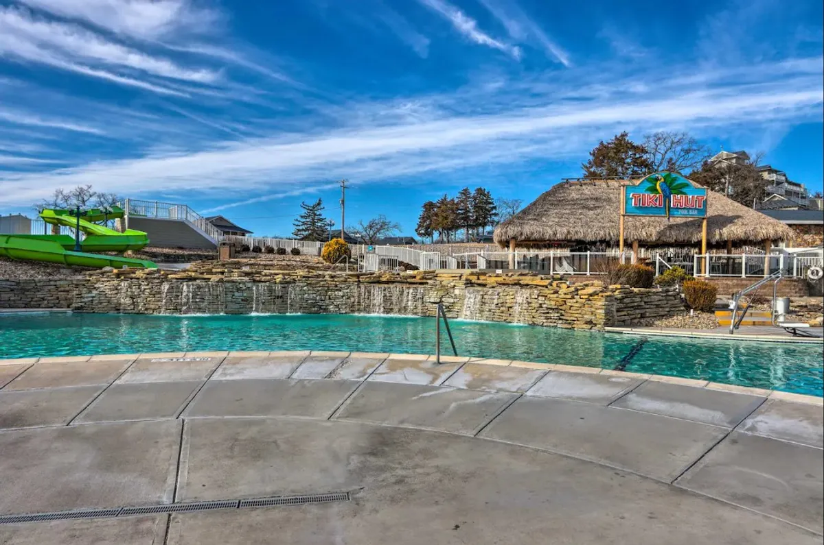 A vibrant exterior scene featuring a resort-style swimming pool with a water slide, Tiki Hut bar, and stone waterfall. The lively area is ideal for swimming, sunbathing, and socializing, capturing the spirit of resort living.