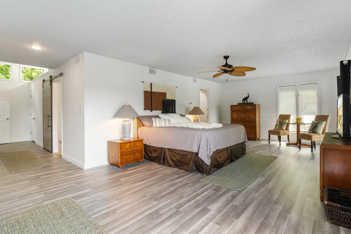A beautifully decorated bedroom with a comfortable bed, a cozy seating area, a dressing table, a lamp casting warm light, and a decorative wall hanging. The room exudes a tranquil, inviting atmosphere perfect for relaxation and rejuvenation.